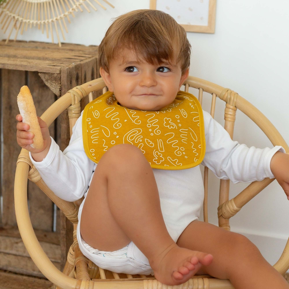 Bebé que se come su babero con su babero mostaza