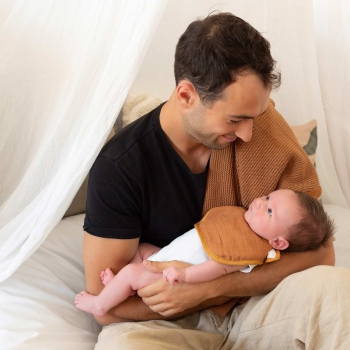 Bébé dans les bras de son papa et qui porte un bavoir terracotta