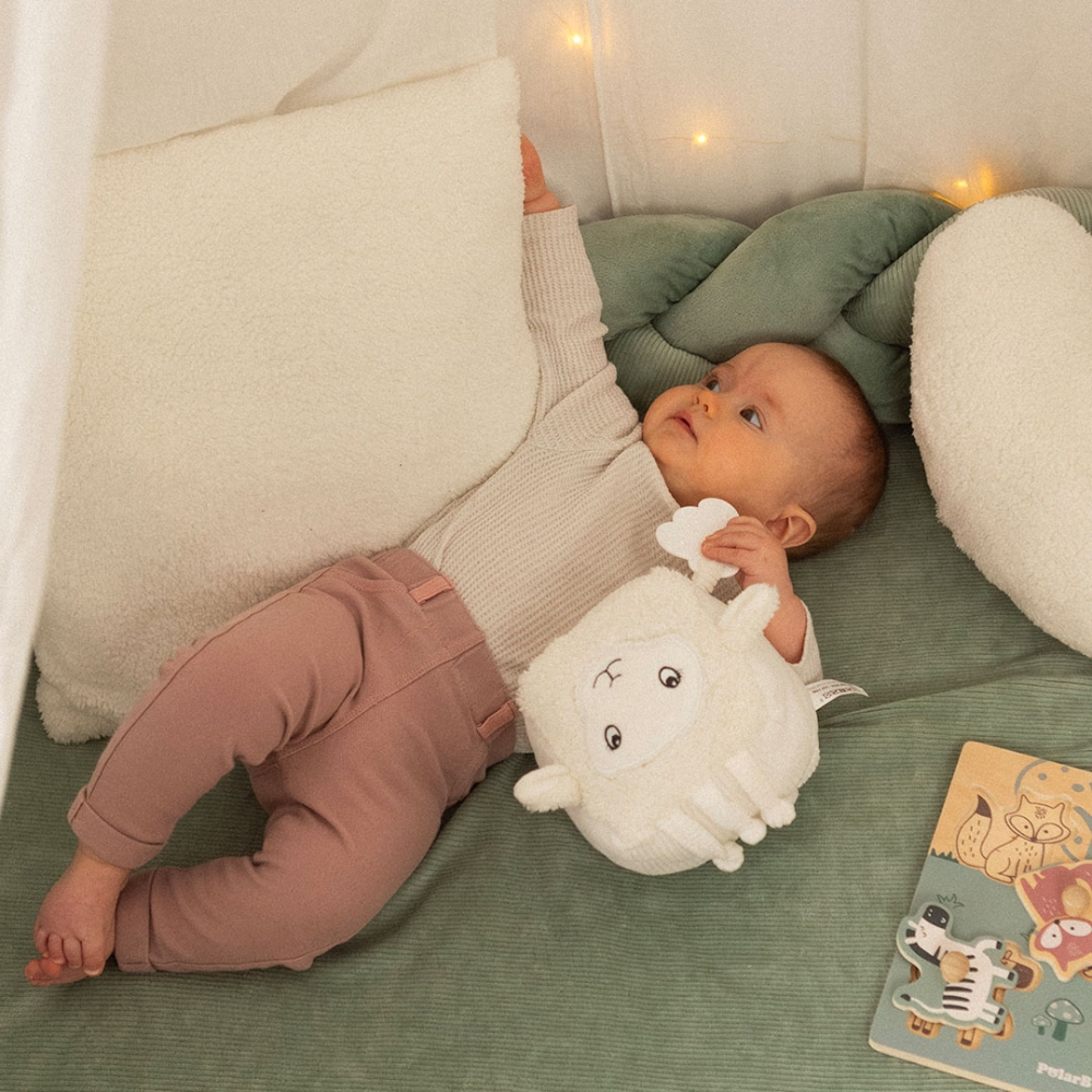 Pequeña bebé niña que juega con el cubo de actividades Wooly la oveja en un rincón de juego