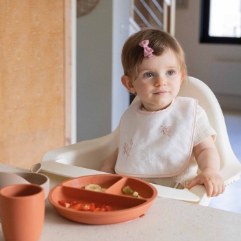 Baby am Tisch mit seinem weißen Lätzchen mit rosa Blumen Baby am Tisch mit seinem weißen Lätzchen mit rosa Blumen