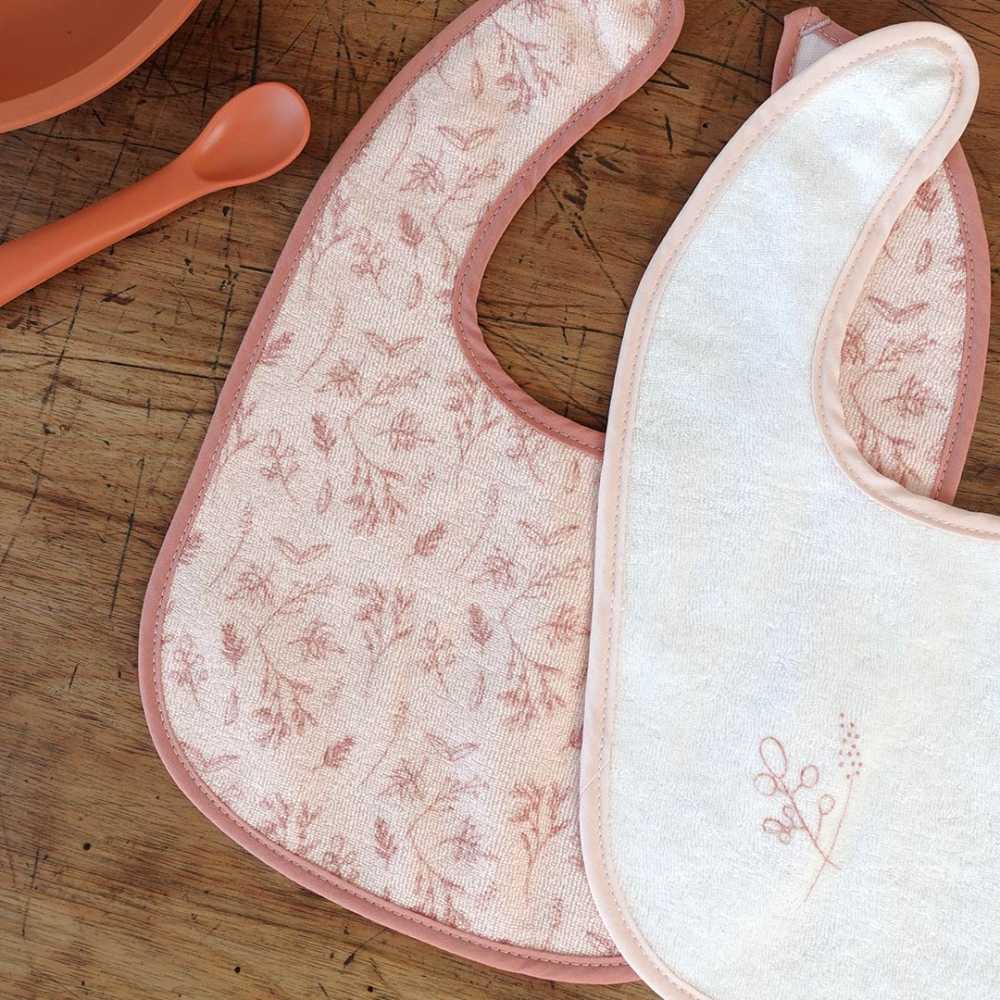 Pormenor dos motivos dos babetes para os primeiros meses em rosa e branco