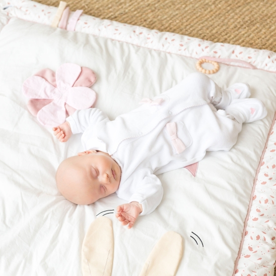 Pink and white play mat with a little baby lying on it