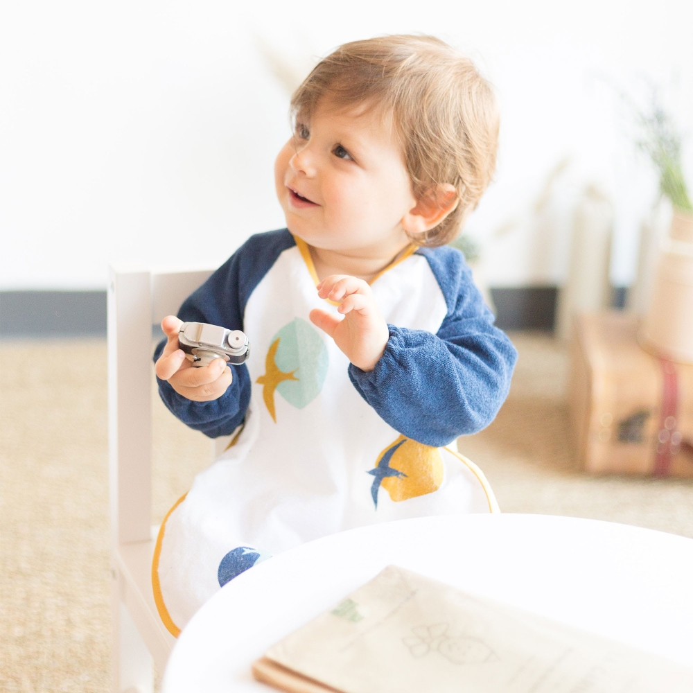 Baby met zijn marineblauw badstof schortslabbetje met mouwen Baby met zijn marineblauw badstof schortslabbetje met mouwen