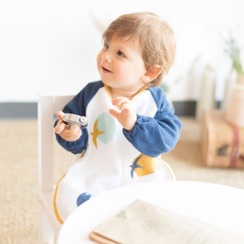 Baby mit seiner Frottee-Schürze mit Ärmeln marineblau Baby mit seiner Frottee-Schürze mit Ärmeln marineblau