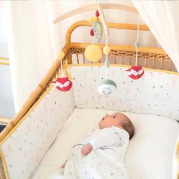 Bebé deitado na cama a olhar para o seu móbile musical, com o resguardo de cama com motivos de bosque Bebé deitado na cama a olhar para o seu móbile musical, com o resguardo de cama com motivos de bosque