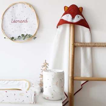 Pequeno saco com produtos para bebé pousado na cómoda, junto à capa de banho com raposa Pequeno saco com produtos para bebé pousado na cómoda, junto à capa de banho com raposa