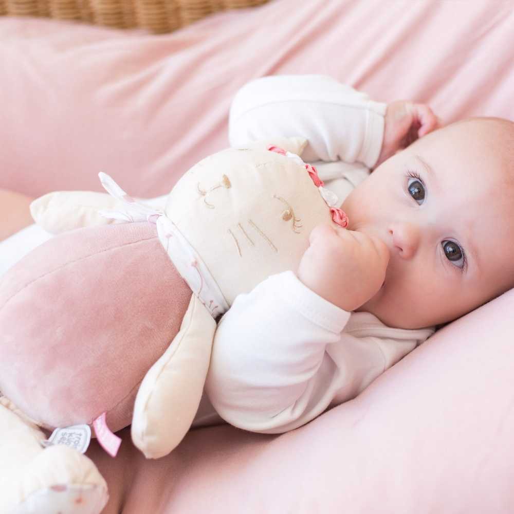 Bebé a adormecer com a sua peluche musical rosa nos braços e o polegar na boca