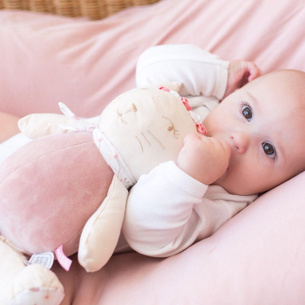 Bebé durmiéndose con su peluche musical Rose en los brazos y su pulgar en la boca
