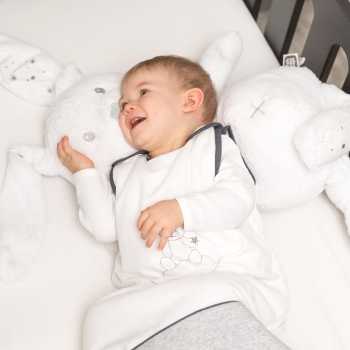O bebé ri com o seu saco de dormir cinzento de 90 cm e o seu grande coelho de peluche O bebé ri com o seu saco de dormir cinzento de 90 cm e o seu grande coelho de peluche