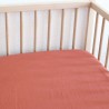 Lençol de baixo ajustável para bebé, liso, em tom terracota, numa cama de madeira Lençol de baixo ajustável para bebé, liso, em tom terracota, numa cama de madeira