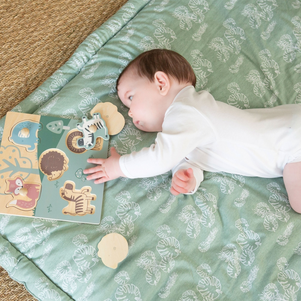 Baby spielt mit seinem Holzpuzzle auf seiner Spielmatte mit Blättermotiv Baby spielt mit seinem Holzpuzzle auf seiner Spielmatte mit Blättermotiv