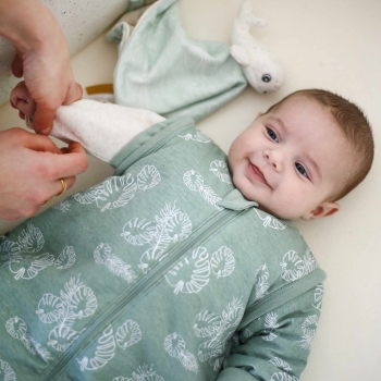 Baby lächelt, während Mama die Ärmel seines grünen Schlafsacks löst Baby lächelt, während Mama die Ärmel seines grünen Schlafsacks löst