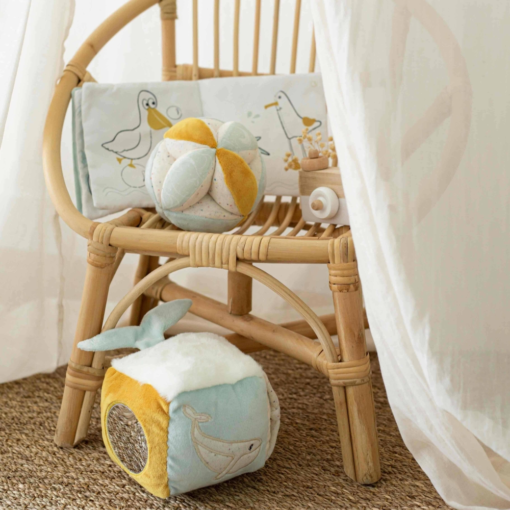 Sensory cube placed on the floor with other developmental toys from the collection on a rattan chair