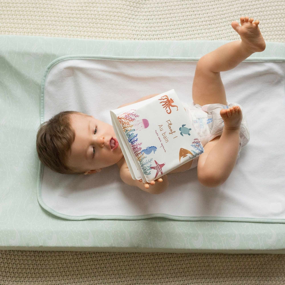 Baby playing with bath book lying in diaper on changing mat Baby playing with bath book lying in diaper on changing mat