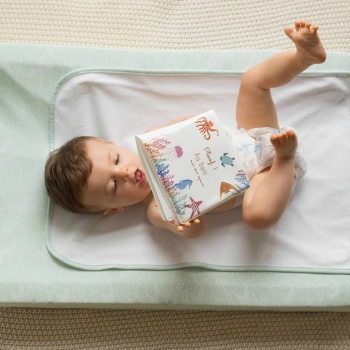 Bébé qui joue avec son livre de bain allongé en couche sur son matelas à langer Bébé qui joue avec son livre de bain allongé en couche sur son matelas à langer