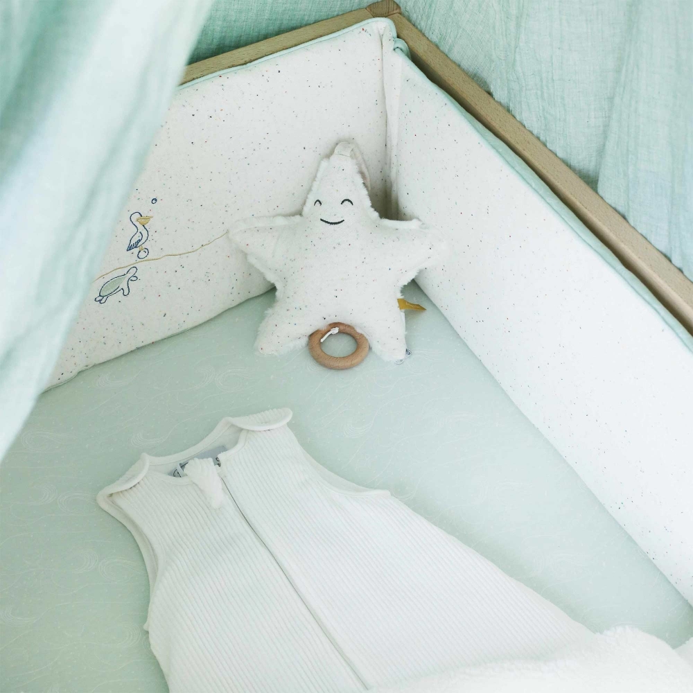 Saco de dormir para recém-nascido numa cama de bebé com decoração de inspiração oceânica Saco de dormir para recém-nascido numa cama de bebé com decoração de inspiração oceânica